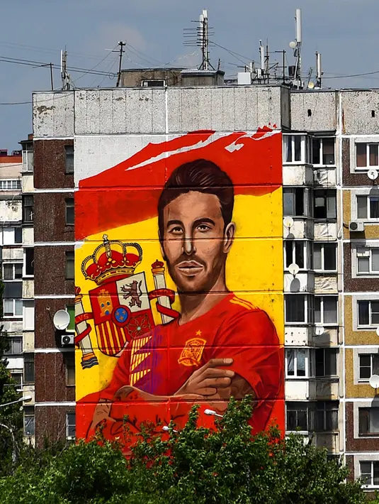 Mural begambar bek Spanyol Sergio Ramos terlihat di sebuah bangunan perumahan di Krasnodar, Rusia, Rabu (6/6). Meski dimusuhi karena perannya dalam cedera Mohamed Salah, Ramos tetap memikat hati pecinta bola Krasnador. (Pierre-Philippe MARCOU/AFP)