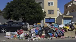 Mobil parkir di dekat tumpukan sampah di sepanjang sisi jalan di Tripoli, ibukota Libya (30/9/2019). Sampah yang berserakan di jalan tersebut menambah cobaan sehari-hari bagi penduduk ibukota yang kehidupannya telah diselingi kekurangan bahan bakar, listrik, dan air. (AFP Photo/Mahmud Turkia)