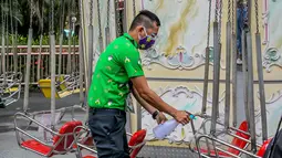 Seorang staf yang mengenakan masker mendisinfeksi wahana di taman hiburan Enchanted Kingdom di Provinsi Laguna, Filipina (18/10/2020). Taman hiburan tersebut kembali dibuka untuk pengunjung. (Xinhua/Rouelle Umali)