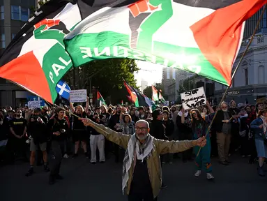 Para pengunjuk rasa mengibarkan bendera dan membawa plakat saat mereka berunjuk rasa selama kunjungan Presiden Israel, Isaac Herzog, di Melbourne, Australia, pada Kamis 12 Februari 2026. Ribuan orang menggelar aksi unjuk rasa di Melbourne, Australia. (WILLIAM WEST/AFP)