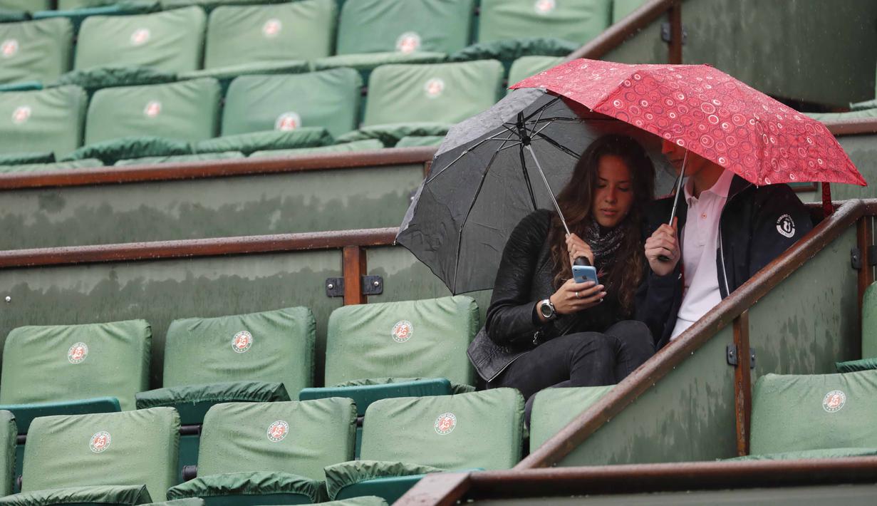 Dua orang penonton menunggu hujan reda  pada laga antara Richard Gasquet dan Kei Nishikori pada turnamen Prancis Terbuka 2016 di Roland Garros, (28/5/2016). (AFP/Thomas Samson)