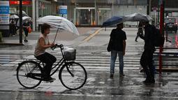 Seorang wanita mengendarai sepeda saat hujan lebat di distrik Akihabara Tokyo (13/8/2022). Hujan lebat yang dibawa oleh Badai Tropis Meari melanda daerah tersebut. (AFP/ Richard A. Brooks)