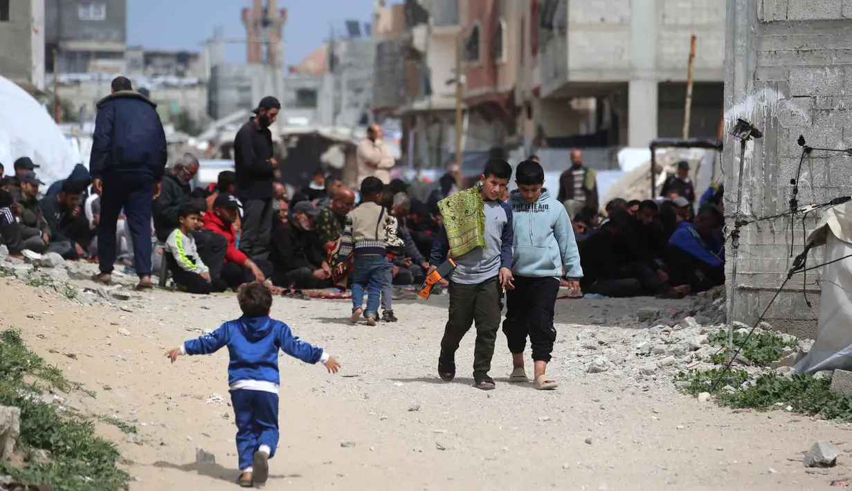 Hari ini dikenal juga sebagai Jumatul Wida atau Jumat perpisahan dengan bulan suci Ramadan. Tampak dalam foto, anak-anak laki-laki Palestina berjalan dengan sajadah mereka sementara para pria Muslim berdoa selama salat Jumat terakhir di bulan suci Ramadan 1447 Hijriah, di luar Masjid Al-Talbani, yang dihancurkan oleh militer Israel di Khan Yunis, Jalur Gaza selatan pada Jumat 13 Maret 2026. (Bashar Taleb/AFP)