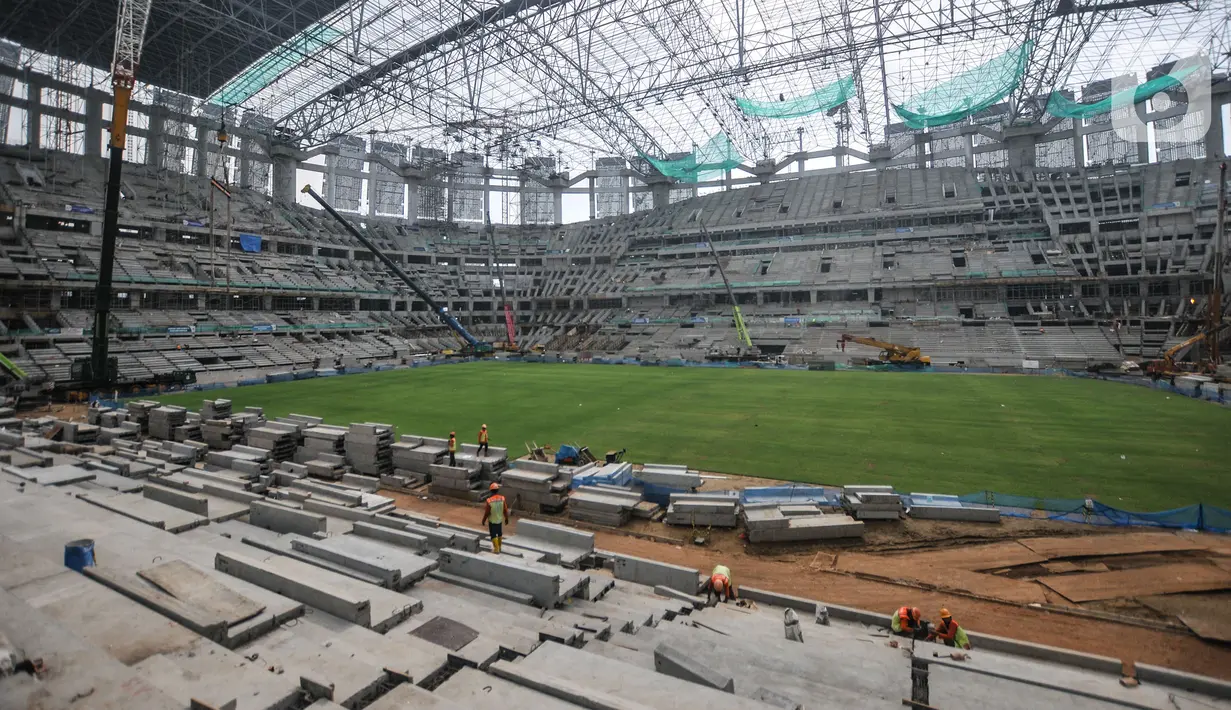 Pekerja menyelesaikan pemasangan rumput di lapangan utama Jakarta International Stadium (JIS), Selasa (26/10/2021). Rumput rekomendasi FIFA ini digadang-gadang mampu digunakan mencapai 1.000 jam pertandingan dalam setahun dan memiliki daya serap air yang baik. (merdeka.com/Iqbal S Nugroho)