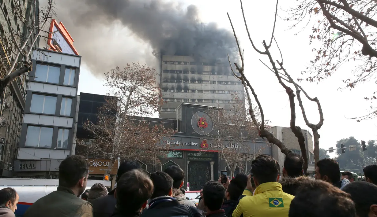 Warga menyaksikan kebakaran yang melanda gedung pencakar langit tertua Iran, gedung Plasco berlantai 15 di pusat kota Teheran, Kamis (19/1). Beberapa bagian bangunan runtuh di tengah upaya pemadam kebakaran menjinakkan api. (AP Photo/Vahid Salemi)