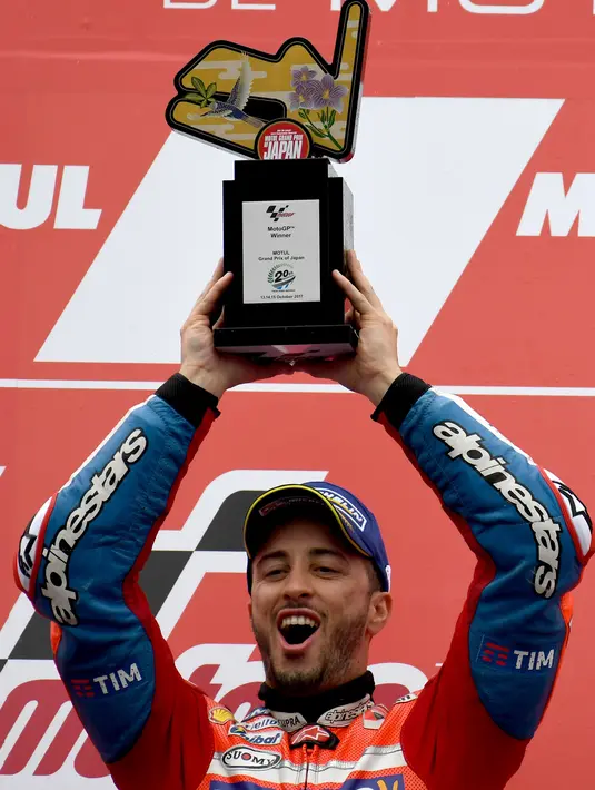 Pembalap Ducati, Andrea Dovizioso mengangkat trofi di podium setelah memenangi MotoGP Jepang di sirkuit Motegi, Minggu (15/10). Dovizioso  juara usai terlibat duel sengit dengan Marc Marquez di tikungan terakhir. (AFP Photo/Toshifumi Kitamura)