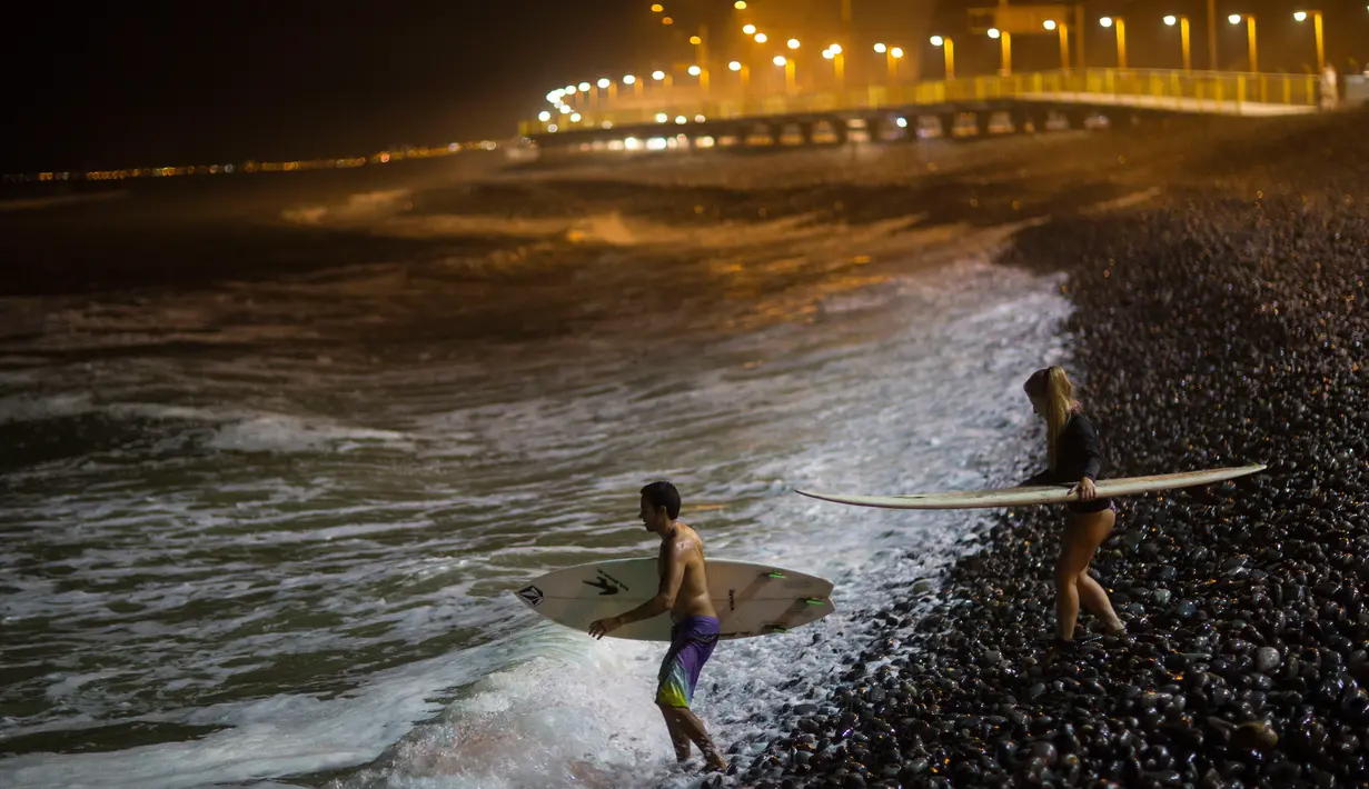 Dua peselancar berjalan di atas bebatuan menuju Samudra Pasifik saat akan berselancar di pantai La Pampilla, ibu kota Peru, Lima, 1 Maret 2017. Sekelompok peselancar hardcore memilih bermain selancar pada malam hari. (AP Photo/Rodrigo Abd)