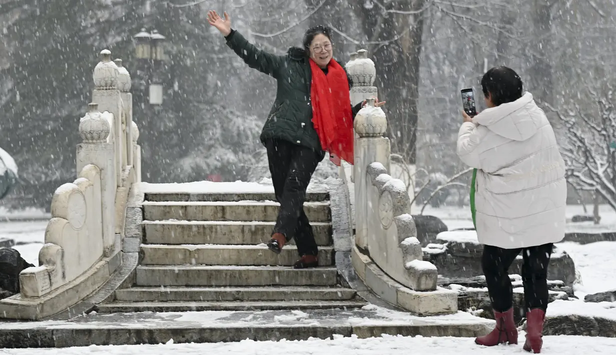 Seorang wanita berpose saat salju turun di sebuah taman di Beijing (16/12/2019). Badai salju dapat membawa kesenangan dan juga masalah bagi penduduk Beijing.  (AFP Photo/Wang Zhao)