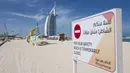 Papan pemberitahuan penutupan pantai terpasang di dekat Burj Al-Arab, Dubai, Uni Emirat Arab, Senin (6/4/2020). Pemerintah Dubai hanya mengizinkan satu orang anggota keluarga bepergian untuk mencari makanan dan obat-obatan. (AP Photo/Jon Gambrell) (AP Photo/Jon Gambrell)