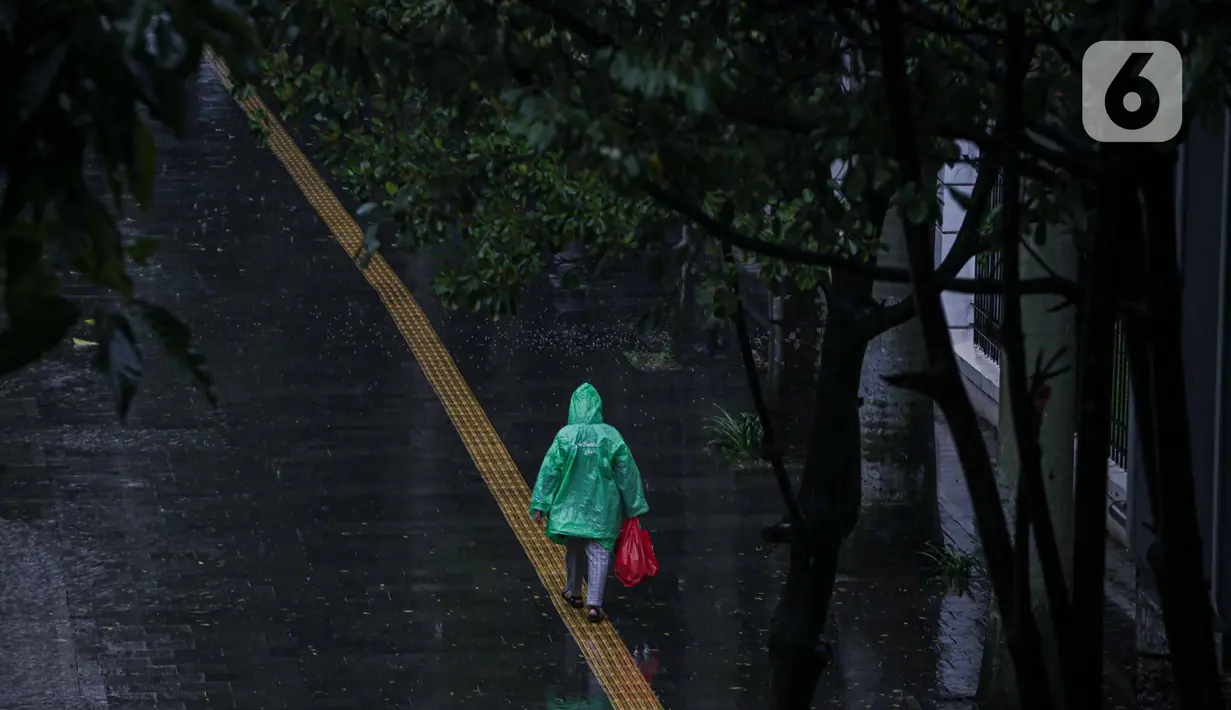 Seorang pejalan kaki mengenakan jas hujan berjalan di kawasan Bundaran HI, Jakarta, Jumat (18/2/2022). BMKG mengungkapkan potensi curah hujan meningkat dan cuaca ekstrem sepanjang 17-23 Februari 2022. Sejumlah wilayah diminta waspada dampak yang terjadi dari cuaca buruk. (Liputan6.com/Faizal Fanani)
