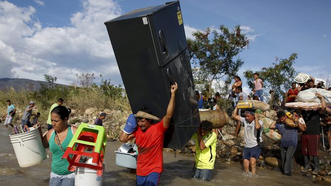 Seorang pria membawa kulkas bersama warga Kolombia lainnya melalui sungai Tachira, Venezuela, (25/8/2015). Pemerintah Venezuela menutup perbatasan dengan Kolombia dan mendeportasi warga Kolombia. (REUTERS/Jose Miguel Gomez)