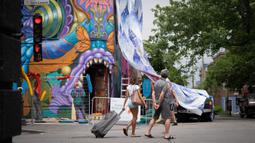 Orang-orang menonton seniman bekerja saat Festival Mural Montreal di Quebec, Kanada, 16 Juni 2022. Dimulai pada tahun 2012, acara seni jalanan itu ingin dinobatkan sebagai "pemimpin seni urban" di Amerika Utara, kata penyelenggara Pierre-Alain Benoit kepada AFP. (Paola Chapdelaine/AFP)