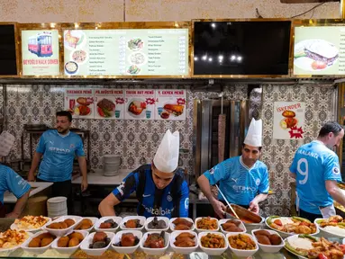 Karyawan sebuah restoran mengenakan kaus Manchester City dan Inter Milan jelang final Liga Champions di Istanbul, Turki, Jumat (9/6/2023). Manchester City akan menghadapi Inter Milan dalam duel perebutan gelar juara Liga Champions di Ataturk Olympic Stadium, Istanbul, Turki, pada 11 Juni 2023 pukul 02.00 WIB. (Umit Turhan Coskun/AFP)