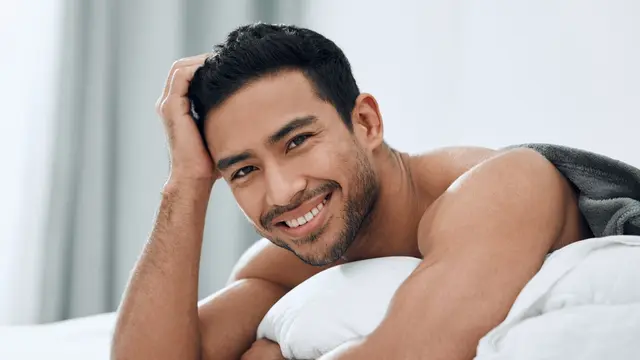 pria tersenyum manis di tempat tidur