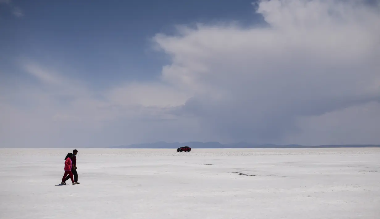 Sepasang suami istri berjalan di Salar de Uyuni, dataran garam terbesar di dunia, di Uyuni, Bolivia, pada 7 November 2020. Dikenal sebagai dataran garam terluas di dunia karena Salar de Uyuni memiliki luas sekitar 4.086 kilometer persegi. (RONALDO SCHEMIDT/AFP)