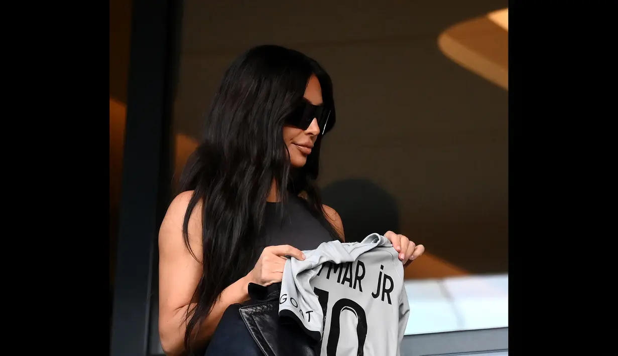 Kim Kardashian berpose dengan jersey milik pemain PSG, Neymar Jr, saat tiba di stadion Parc des Princes untuk menyaksikan pertandingan Ligue 1 antara PSG melawan Rennais, Minggu (19/3/2023) malam WIB. (AFP/Frank Fife)