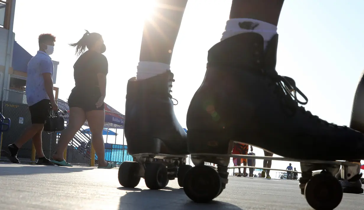 Orang-orang yang mengenakan masker berjalan dekat sepatu roda di Santa Monica, California, Kamis (3/9/2020). Permintaan sepatu roda di Amerika Serikat mengalami peningkatan tajam untuk mencari aktivitas di luar ruangan di tengah pembatasan sosial akibat corona Covid-19. (Mario Tama/Getty Images/AFP)