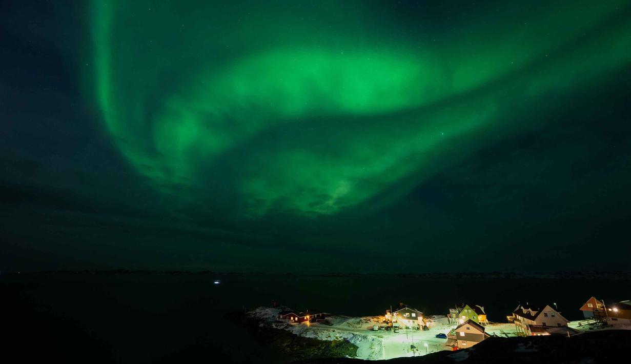 Fenomena ini juga hanya bisa dilihat di lokasi dan pada waktu tertentu. Tampak dalam foto, Aurora Borealis menerangi langit malam di atas rumah-rumah penduduk di Nuuk, Greenland, pada 23 Januari 2026. (Jonathan NACKSTRAND/AFP)