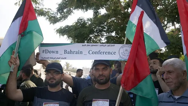 Warga Palestina di Kota Gaza pada 24 Juni 2019, mengibarkan bendera nasional dan memegang spanduk yang mengecam konferensi Perdamaian untuk Kemakmuran yang dipimpin AS di Bahrain. (MOHAMMED ABED / AFP)