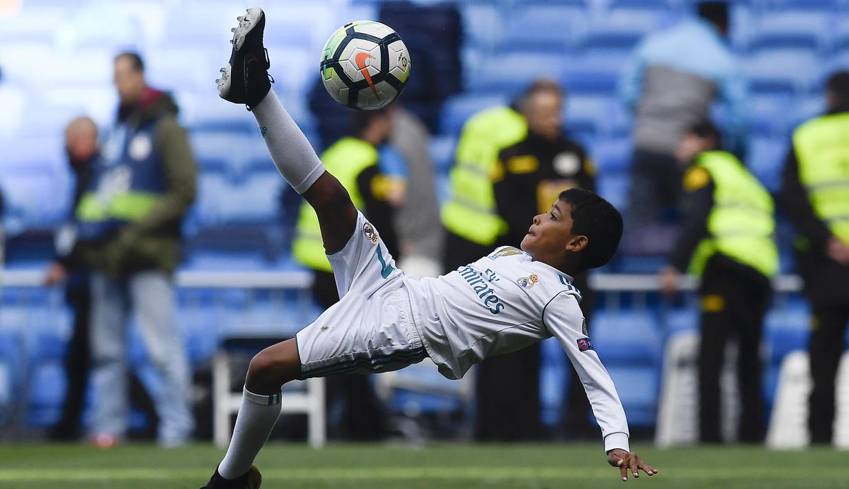 Putra dari Cristiano Ronaldo melakukan tendangan salto saat menemani sang ayah di Stadion Santiago Bernabeu, Madrid, Minggu (8/4/2018). Tendangan ini mirip seperti saat CR 7 membobol gawang Juventus. (AFP/Gabriel Bouys).