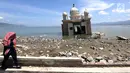 Warga melintas di depan Masjid Terapung Arqam Bab Al Rahman pasca gempa dan tsunami Palu di Pantai Talise, Sulawesi Tengah. Bangunan masjid yang terletak di pinggir pantai terlihat utuh meski sebagian bangunannya tenggelam. (Liputan6.com/Fery Padolo)