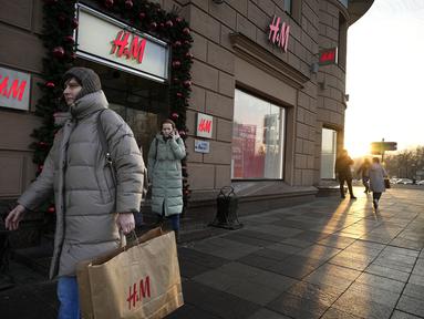 Seorang perempuan membawa kantong belanja setelah meninggalkan toko utama H&M di Moskow, Rusia, Rabu (30/11/2022). Pengecer mode no.2 dunia itu akhirnya menutup semua tokonya di Rusia untuk selamanya. (AP Photo/Alexander Zemlianichenko)