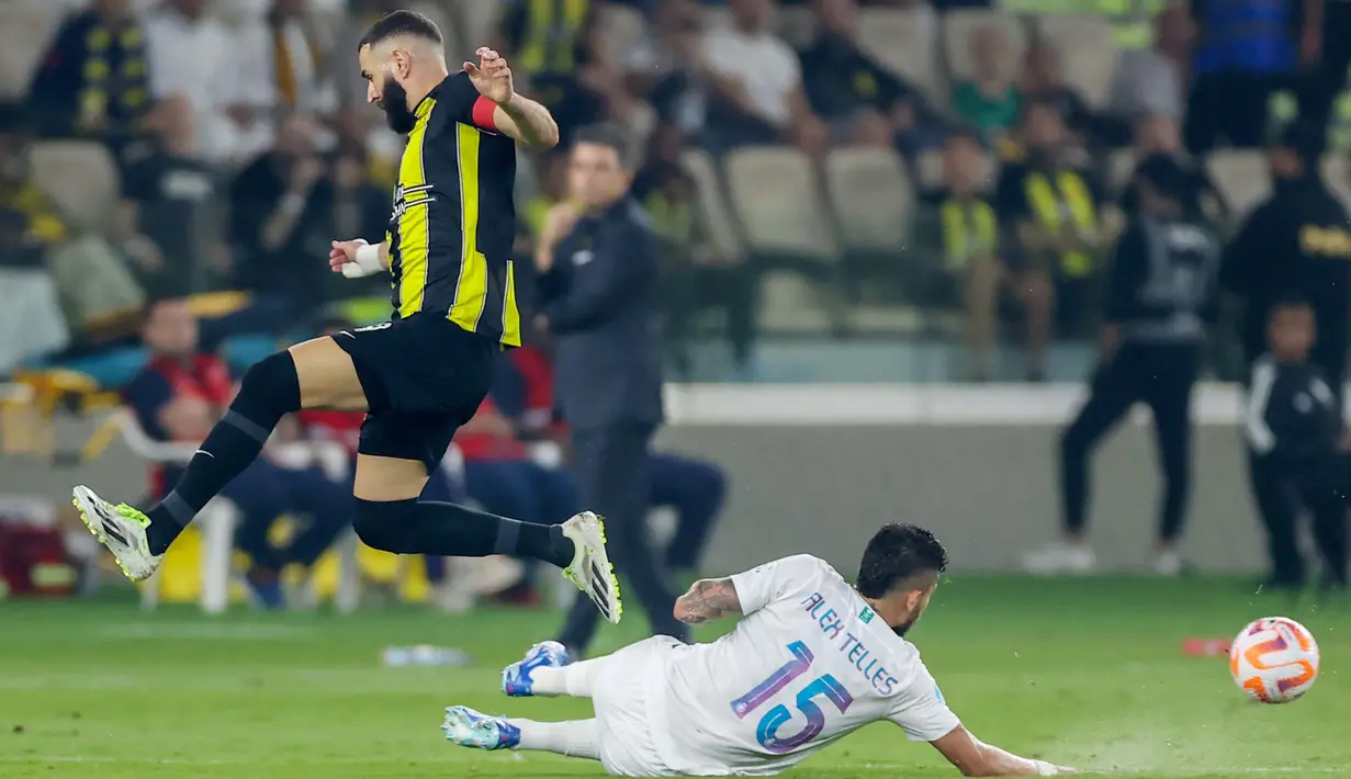 Pemain Al Ittihad, Karim Benzema, berusaha melewati pemain Al Nassr, Alex Telles, dalam laga tunda pekan ke-17 Liga Arab Saudi di King Abdullah Sport City Stadium, Jeddah, Rabu (27/12/2023). Laga ini dihiasi para mantan pemain bintang di Eropa. (Photo by AFP)