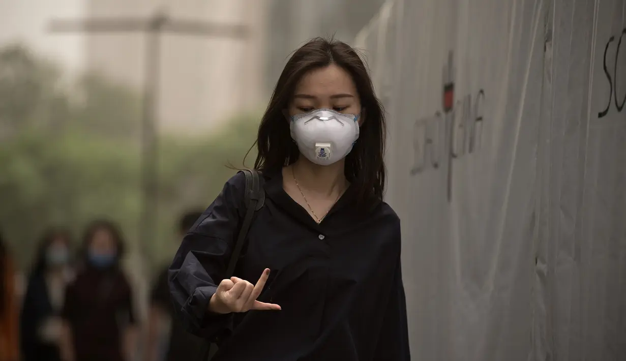 Seorang wanita berjalan sambil mengenakan masker saat badai debu menerjang kota Beijing, China, Kamis (4/5). Diperkirakan, badai deb akan mencakup sebagian besar wilayah barat laut China. (Nicolas ASFOURI/AFP)