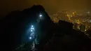 Demonstran antipemerintah membawa patung The Lady Liberty of Hong Kong untuk didirikan di puncak pegunungan Lion Rock, Hong Kong, Minggu (13/10/2019). Beberapa di antara demonstran mengenakan lampu kepala meski badai petir melanda semalaman. (AP Photo/Kin Cheung)