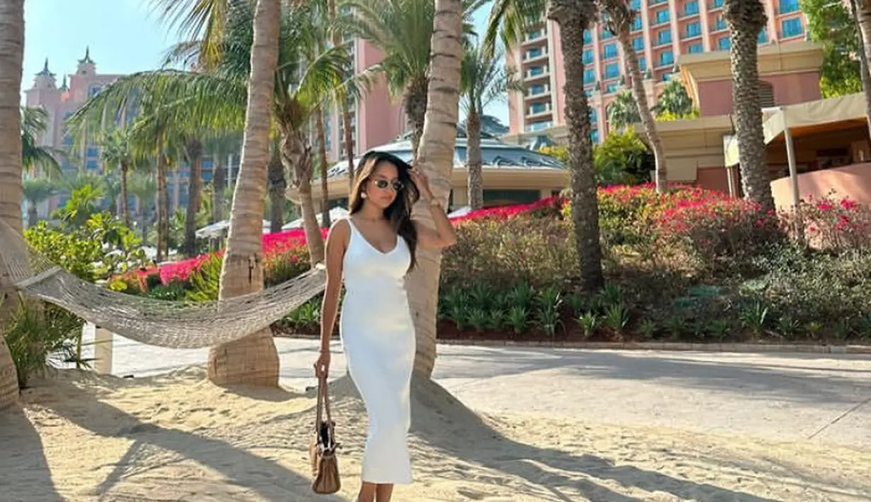 Jennifer juga tampil mengenakan dress putih panjang spaghetti strap. Dipadukan sandal sambil membawa tas coklat. Ia pun tampil mengenakan kacamata hitam. [@jennifercoppenreal20]