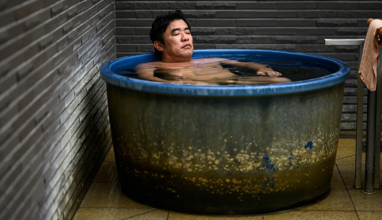 Masazumi Kato bersantai dalam bak mandi di pemandian air panas Jepang atau onsen di Yokohama, prefektur Kanagawa pada 29 Mei 2020. Dengan pencabutan status darurat nasional pada Senin (25/5) lalu, banyak bisnis yang mulai beroperasi kembali tak terkecuali dengan onsen. (Behrouz MEHRI/AFP)