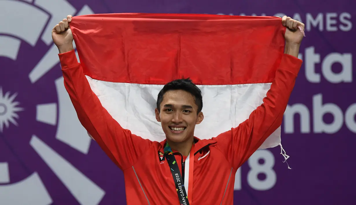 Jonatan Christie tersenyum sambil mengibarkan bendera Merah Putih saat upacara penghargaan cabang olahraga badminton Asian Games 2018, Jakarta, Selasa (28/8). Jonatan menang tiga set langsung 21-18, 20-22, dan 21-15. (AFP Photo/Sonny Tumbelaka)