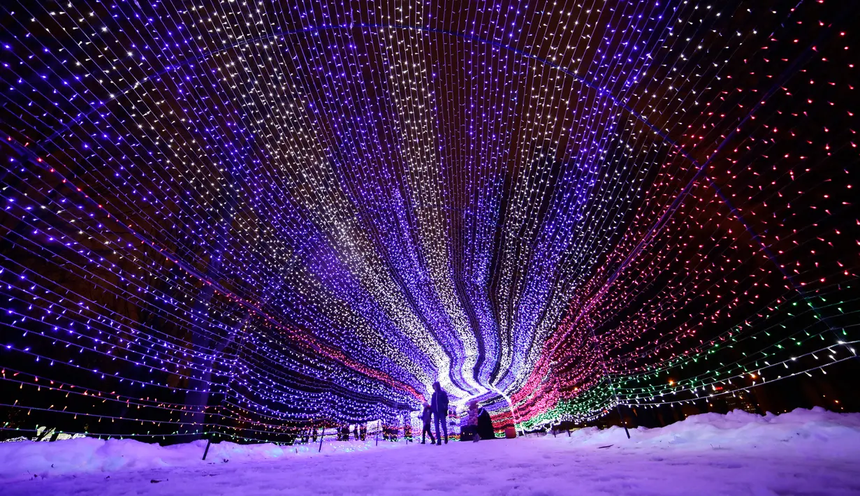 Pengunjung berjalan di dalam hiasan cahaya lampu di sebuah taman di Minsk, Belarus (28/12). Setelah matahari terbenam, orang-orang berdatangan untuk menikmati pameran cahaya lampu yang dipasang di seluruh taman. (AP Photo/Grits Sergei)