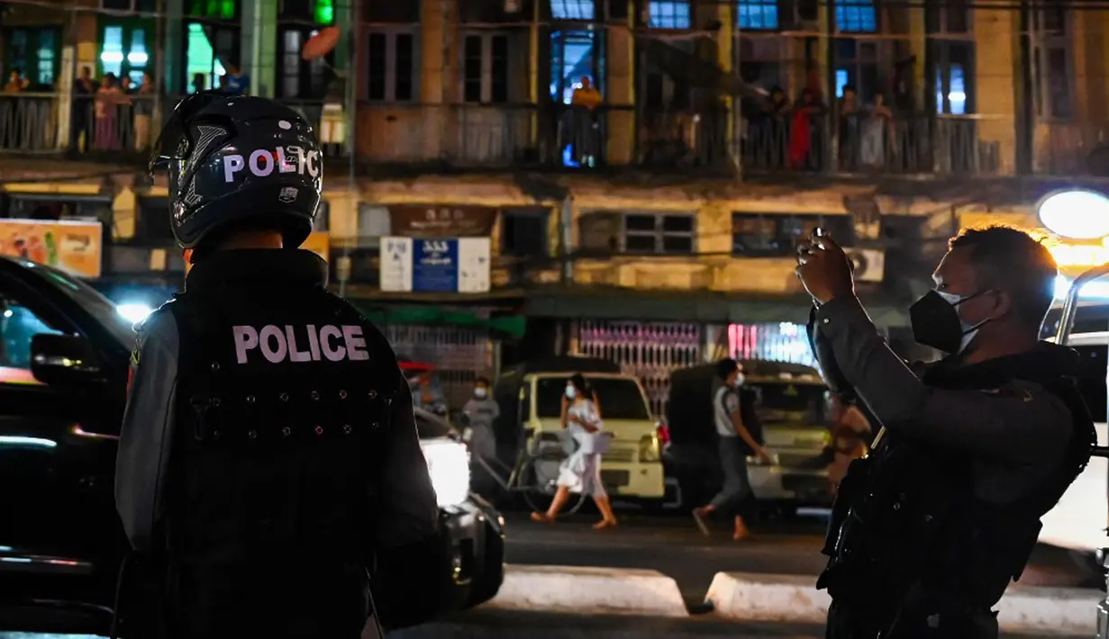 Polisi merekam dengan ponsel saat orang-orang membuat keributan setelah seruan untuk protes keluar di media sosial di Yangon, Myanmar, 3 Februari 2021. Kudeta militer Myanmar terus memicu protes warga dengan membunyikan klakson mobil, menyalakan lampu ponsel, dan memukul-mukul panci. (STR/AFP)