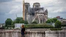 Seorang wanita mengamati Katedral Notre-Dame yang tengah dipugar di Paris, Prancis, Senin (27/4/2020). Renovasi Katedral Notre-Dame dilanjutkan kembali setelah sempat dihentikan sejak 17 Maret lalu akibat epidemi COVID-19. (Xinhua/Aurelien Morissard)
