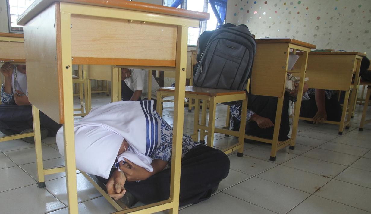 Anak-anak sekolah berada di bawah meja saat berpartisipasi dalam latihan tsunami di Meulaboh, Aceh, (5/9). Latihan ini menyimulasikan gempa berkekuatan 9,3 di lepas pantai barat pulau Sumatra di Indonesia. (AFP Photo/Januar)