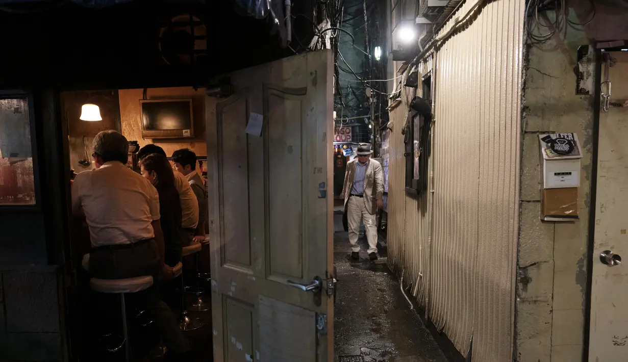 Seorang pria berjalan melalui lorong sempit antara dua bangunan di Golden Gai di distrik Shinjuku, Tokyo (17/7/2019). Di area ini, pengambilan foto dan video untuk semua keperluan di jalan dilarang tanpa izin dari asosiasi promosi bisnis di daerah tersebut. (AP Photo / Jae C. Hong)