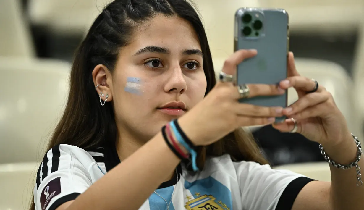 Seorang fans wanita Argentina menggunakan ponselnya di tribun jelang pertandingan semifinal Piala Dunia Qatar 2022 antara Argentina dan Kroasia di Stadion Lusail di Lusail, utara Doha, Rabu (14/12/2022). (AFP/Jewel Samad)
