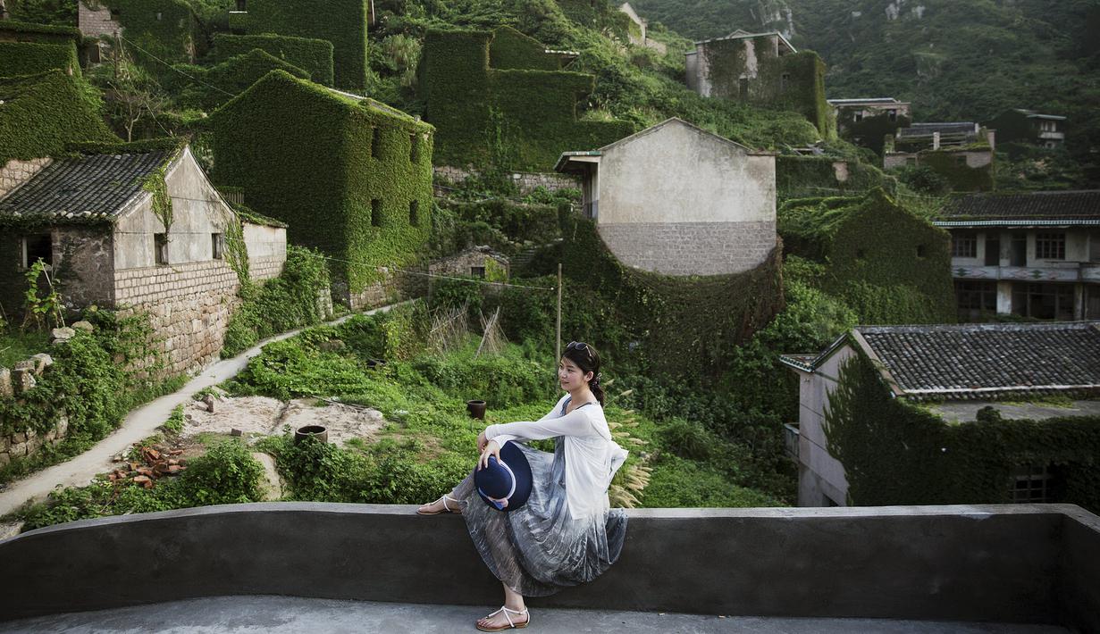 Seorang wisatawan berfoto dengan latar belakang sebuah desa yang sudah ditinggalkan penghuninya, di Houtouwan, pulau Shengshan, China, 26 Juli 2015. Desa ini dulunya dihuni lebih dari 2.000 nelayan. (REUTERS/Damir Sagolj)
