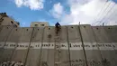 Seorang pria Palestina menggunakan tangga memanjat tembok Israel yang kontroversial saat akan salat Jumat pertama Ramadan di masjid Al-Aqsa, Yerusalem (10/5/2019). (Reuters/Mohamad Torokman)