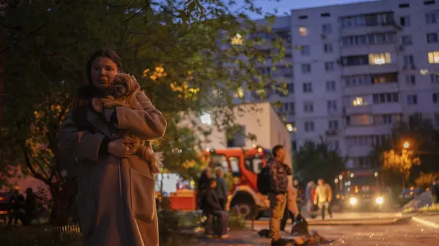 Seorang wanita menggendong anjingnya saat berjalan di jalan yang dipenuhi pecahan kaca di lokasi bangunan tempat tinggal yang rusak setelah serangan Rusia di Kyiv, Ukraina, Sabtu, 24 Mei 2025. (AP/Alex Babenko)