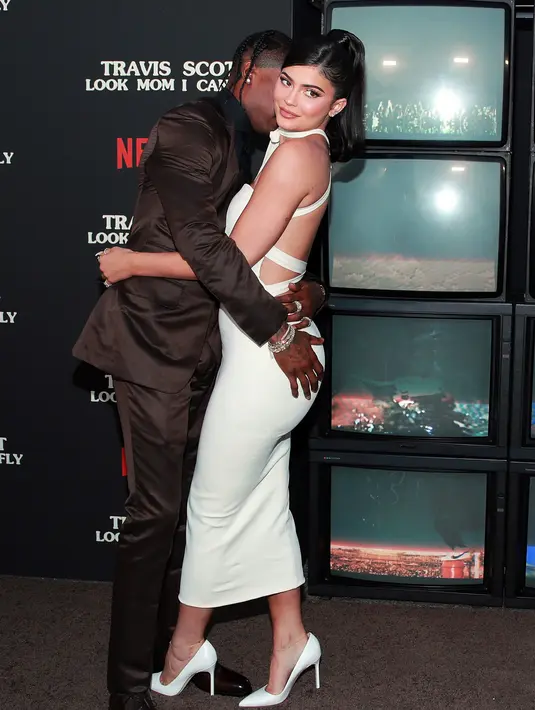 Travis Scott (kiri) mencium dan memeluk Kylie Jenner saat menghadiri pemutaran perdana Netflix "Travis Scott: Look Mom I Can Fly" di Barker Hangar, Santa Monica, California, Amerika Serikat, Senin (27/8/2019). Kylie mengenakan gaun putih dan sepatu glamor. (Rich Fury/GETTY IMAGES NORTH AMERICA/AFP)