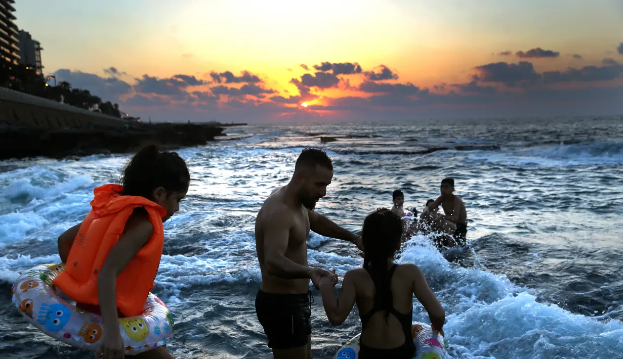 Seorang pria bersama dua putrinya berenang di Laut Mediterania dari Corniche, atau promenade tepi laut, saat matahari terbenam pada hari terakhir musim panas, di Beirut, Lebanon (20/9). (AP Photo / Hussein Malla)