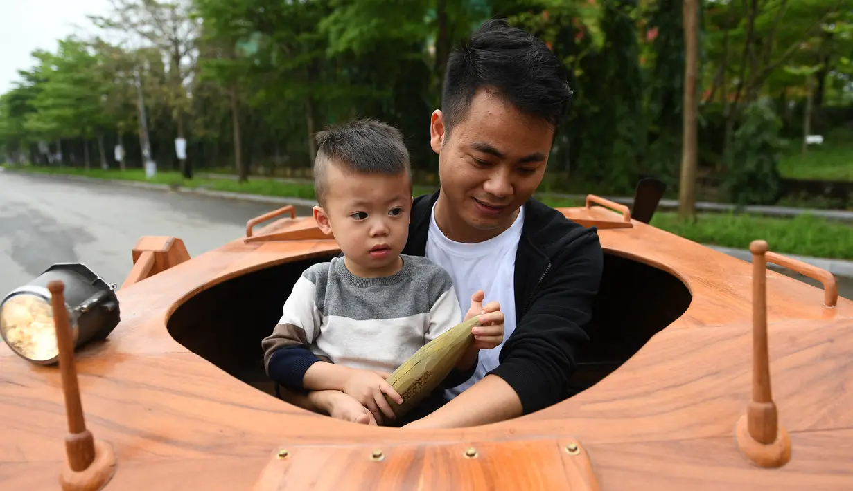 Truong Van Dao dan putranya menaiki tank kayu di daerah perumahan di provinsi Bac Ninh pada 28 Maret 2022. Seorang ayah di Vietnam telah menghabiskan ratusan jam dan menginvestasikan uangnya untuk mengubah mobil van tua menjadi tank kayu untuk putranya. (Nhac NGUYEN /AFP)