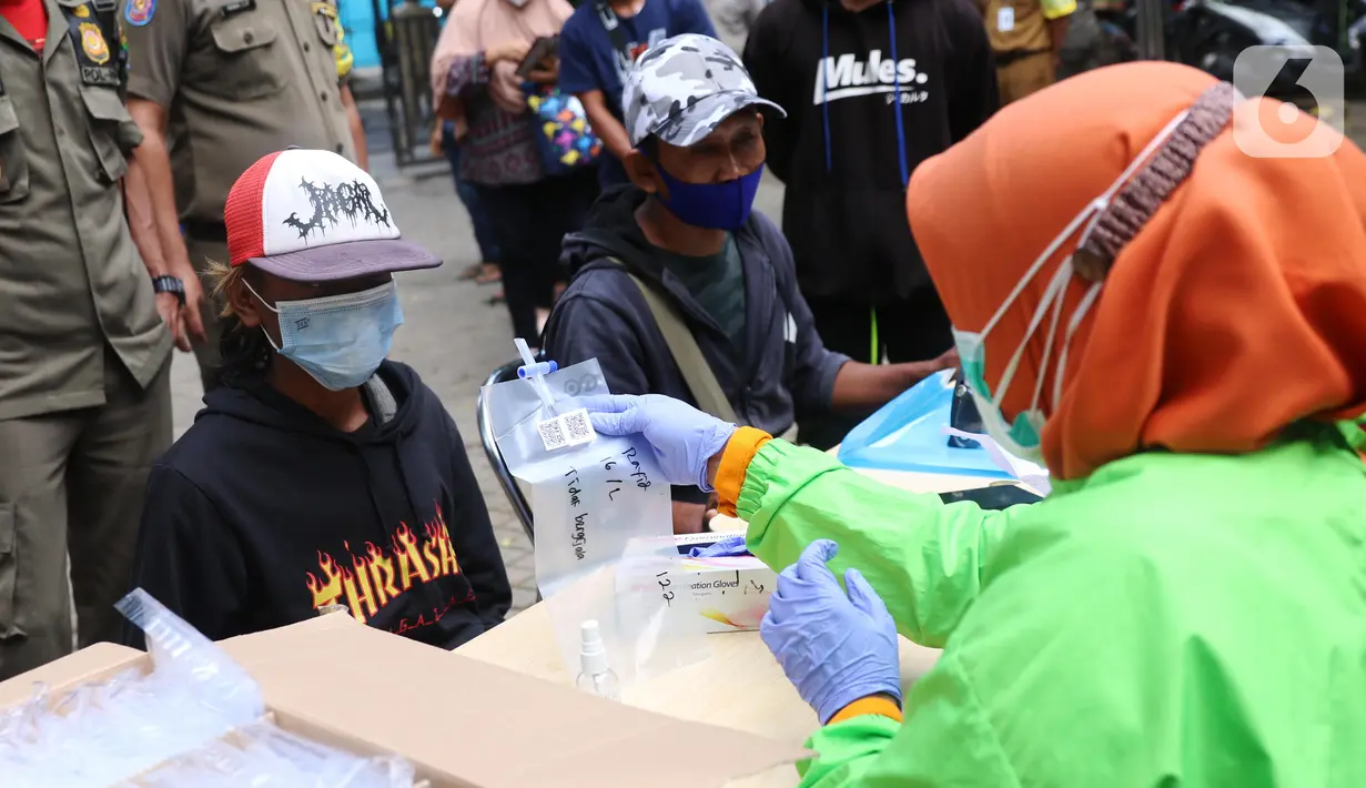 Petugas memberikan kantong kepada warga untuk menjalani tes GeNose C19 usai terjaring razia penggunaan masker di Kelurahan Sudimara Barat, Kota Tangerang, Kamis (27/5/2021). Tes tersebut untuk menekan penyebaran corona COVID-19 di wilayah tersebut. (Liputan6.com/Angga Yuniar)