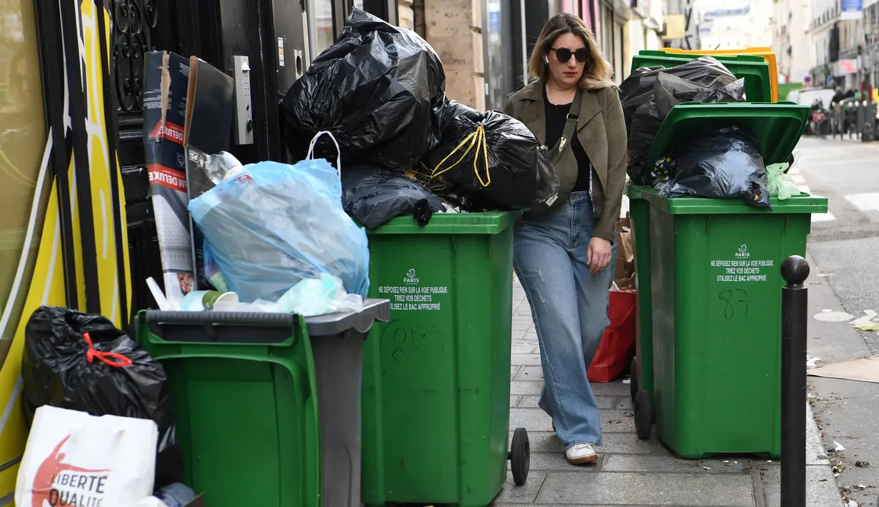 Seorang pejalan kaki berjalan di antara tempat sampah yang penuh di distrik ke-2 Paris saat petugas kebersihan mogok menentang reformasi pensiun, membuat banyak jalan di ibu kota penuh dengan sampah yang berbau busuk, Kamis (17/3/2023). (Photo by Bertrand GUAY / AFP)