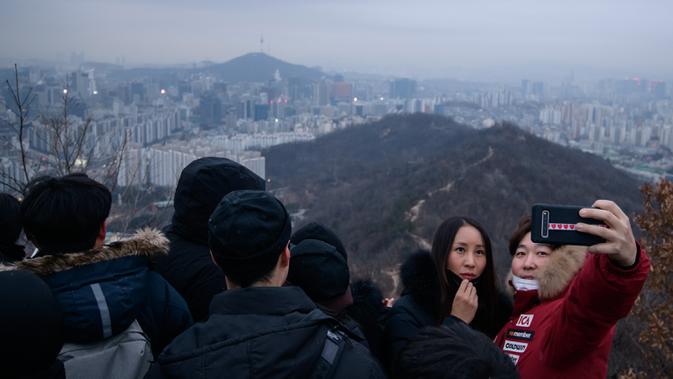 Pasangan berselfie di sudut pandang yang menghadap ke cakrawala kota untuk menyaksikan matahari terbit pertama tahun baru, meskipun dalam kondisi mendung, di Seoul, Korea Selatan (1/1/2020). (AFP/Ed Jones)