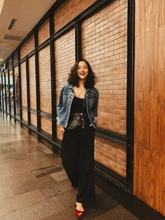 Jumpsuit hitam yang dipadukan dengan jaket denim adalah busana yang tepat untuk bergaya santai. Aksesoris sling bag dan sepatu merah, membuat gaya presenter sekaligus aktor ini terlihat ciamik.  (Liputan6.com/IG/@putrimarino)
