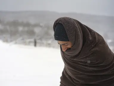 Seorang migran dengan dibungkus selimut berjalan melewati salju di kamp Lipa, barat daya Bosnia, dekat perbatasan dengan Kroasia, Sabtu (26/12/2020). Ratusan migran terdampar di tenda-tenda kumuh dan terbakar di Bosnia, di tengah hujan salju yang lebat dan suhu membeku. (AP Photo/Kemal Softic)