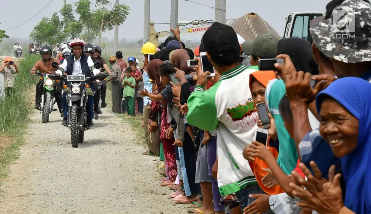 Warga menyambut kedatangan Presiden Joko Widodo saat mengendarai motor trail di Muara Gembong, Bekasi (1/11). Jokowi mengenakan kemeja putih, celana jeans, dengan balutan jaket rompi berwarna hitam. (Liputan6.com/Biro Pers Kepresidenan/Agus Suparto)